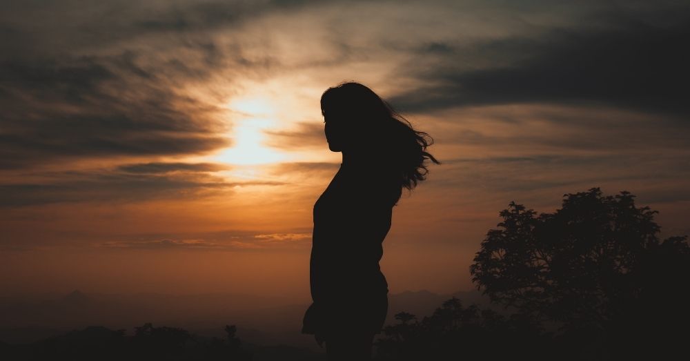 This is an image of a woman standing against the sunset